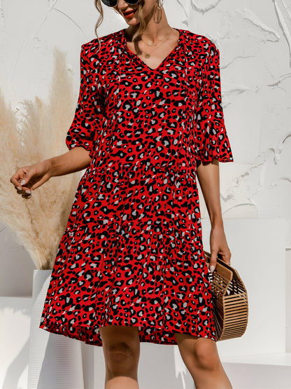 Red - Model wearing a woven leopard print v-neck tiered mini dress with flutter sleeves and neckline tie details, holding a structured bamboo handbag.