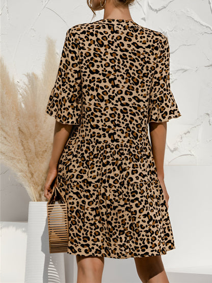 Leopard - Model wearing a woven leopard print v-neck tiered mini dress with flutter sleeves and neckline tie details, holding a structured bamboo handbag.