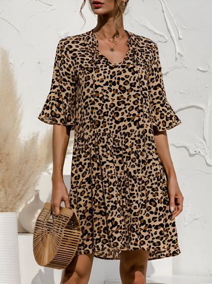 Leopard - Model wearing a woven leopard print v-neck tiered mini dress with flutter sleeves and neckline tie details, holding a structured bamboo handbag.