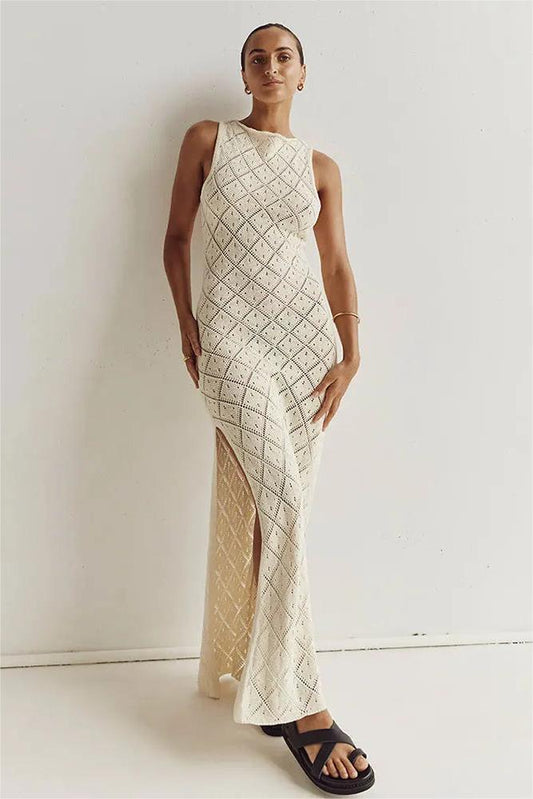 White - A woman modelling a cream-coloured, sleeveless maxi dress featuring an intricate geometric open-knit pattern, a high neckline, and a high side slit.