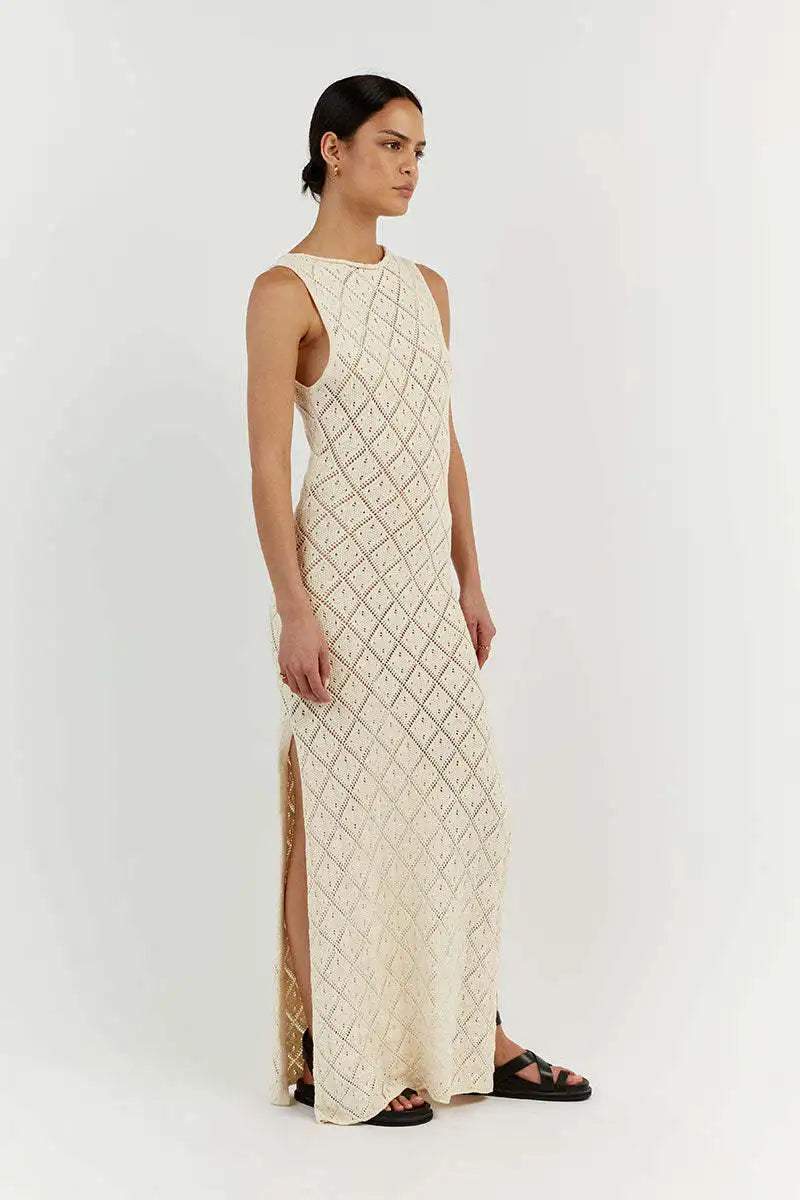 White - A woman modelling a cream-coloured, sleeveless maxi dress featuring an intricate geometric open-knit pattern, a high neckline, and a high side slit.