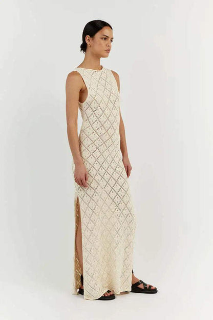 White - A woman modelling a cream-coloured, sleeveless maxi dress featuring an intricate geometric open-knit pattern, a high neckline, and a high side slit.