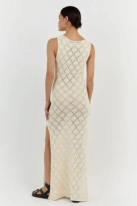 White - A woman modelling a cream-coloured, sleeveless maxi dress featuring an intricate geometric open-knit pattern, a high neckline, and a high side slit.
