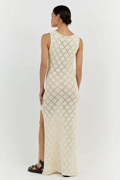 White - A woman modelling a cream-coloured, sleeveless maxi dress featuring an intricate geometric open-knit pattern, a high neckline, and a high side slit.