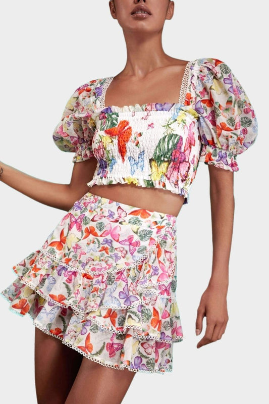 White - Women's white cropped blouse featuring a colourful butterfly and botanical print, a shirred bodice, square neckline, and short puff sleeves, paired with a matching tiered mini skirt.