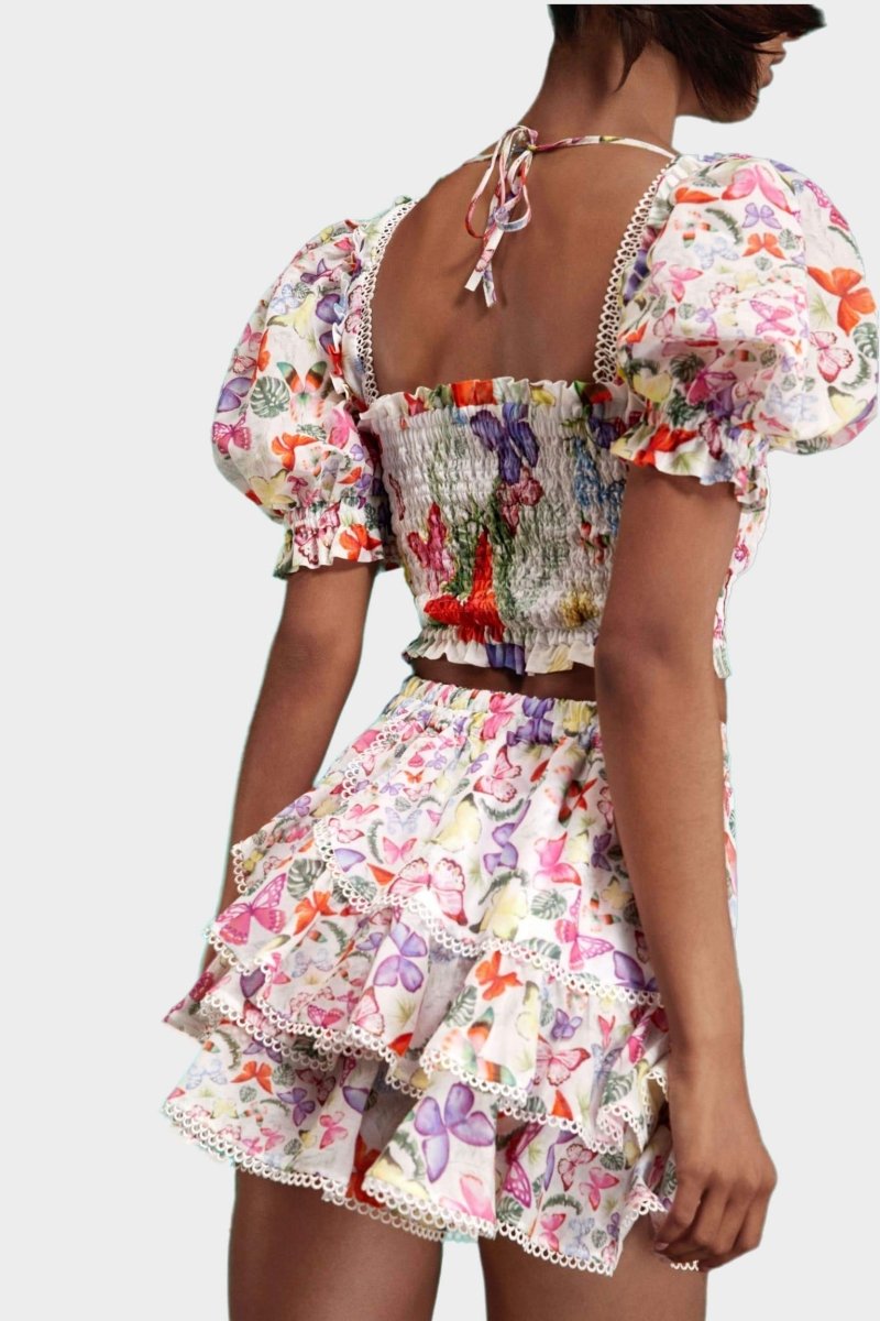 White - Women's white cropped blouse featuring a colourful butterfly and botanical print, a shirred bodice, square neckline, and short puff sleeves, paired with a matching tiered mini skirt.