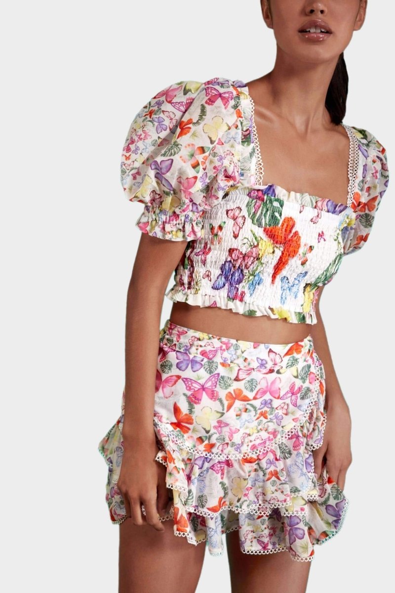 White - Women's white cropped blouse featuring a colourful butterfly and botanical print, a shirred bodice, square neckline, and short puff sleeves, paired with a matching tiered mini skirt.