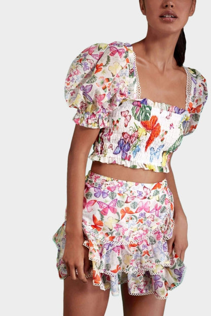 White - Women's white cropped blouse featuring a colourful butterfly and botanical print, a shirred bodice, square neckline, and short puff sleeves, paired with a matching tiered mini skirt.