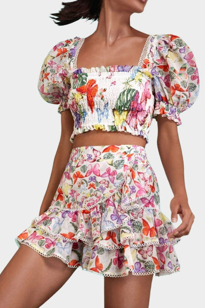 White - Women's white cropped blouse featuring a colourful butterfly and botanical print, a shirred bodice, square neckline, and short puff sleeves, paired with a matching tiered mini skirt.