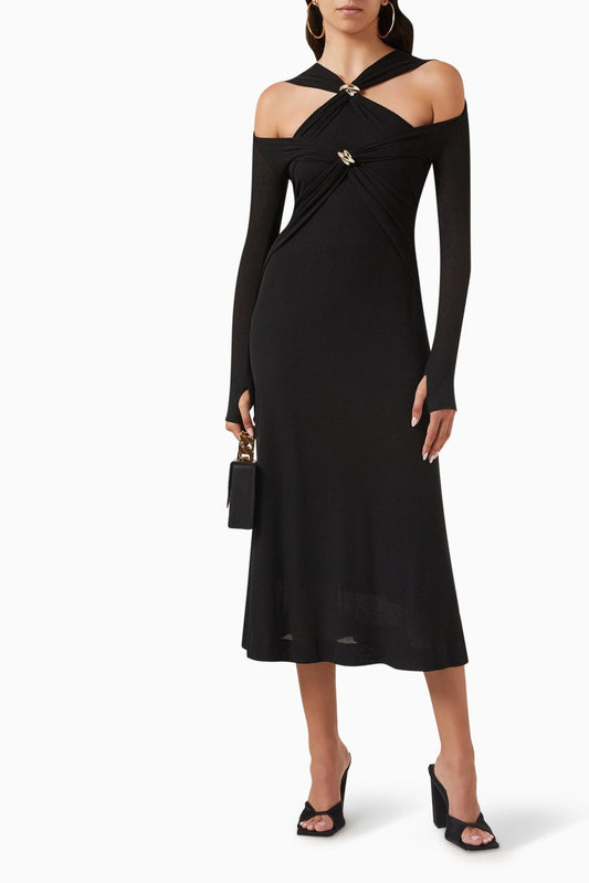 Black - Full-length view of a model in a black knit midi dress with a twisted halter neckline, cold-shoulder cutouts, long fitted sleeves, and gold hardware embellishments.
