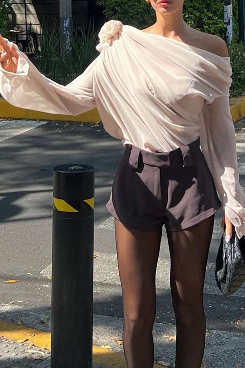 Beige - A woman wearing an elegant, cream-coloured, one-shoulder draped blouse featuring a large 3D floral appliqué on the right shoulder and a single long sleeve.