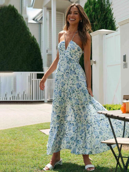 Blue - A woman wearing a white maxi dress with an orange and blue floral print, featuring a halter neckline, ruched bodice, and tiered skirt, standing outdoors.