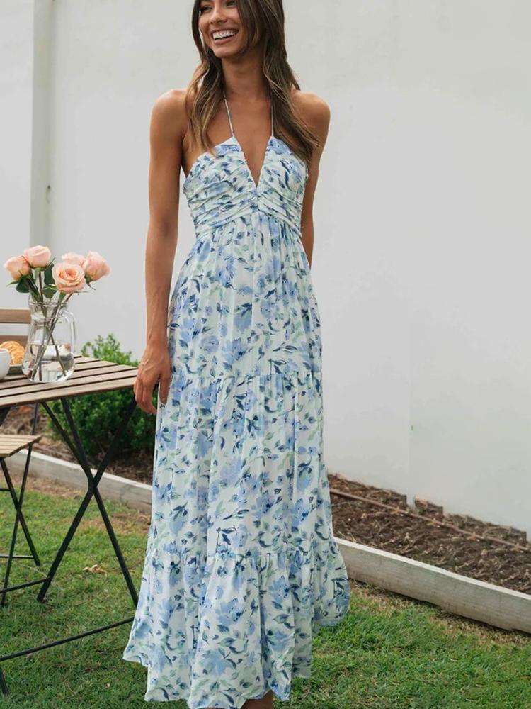 Blue - A woman wearing a white maxi dress with an orange and blue floral print, featuring a halter neckline, ruched bodice, and tiered skirt, standing outdoors.