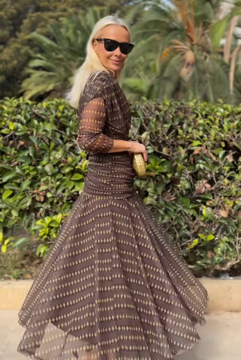 Brown - A woman smiling outdoors wearing an elegant, flowing brown maxi dress with a geometric diamond print, featuring a wrap-style V-neckline, sheer 3/4 sleeves, and a full skirt.