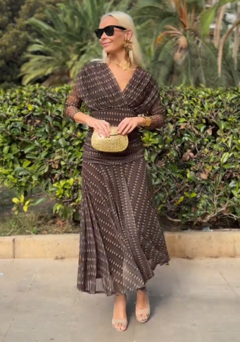 Brown - A woman smiling outdoors wearing an elegant, flowing brown maxi dress with a geometric diamond print, featuring a wrap-style V-neckline, sheer 3/4 sleeves, and a full skirt.