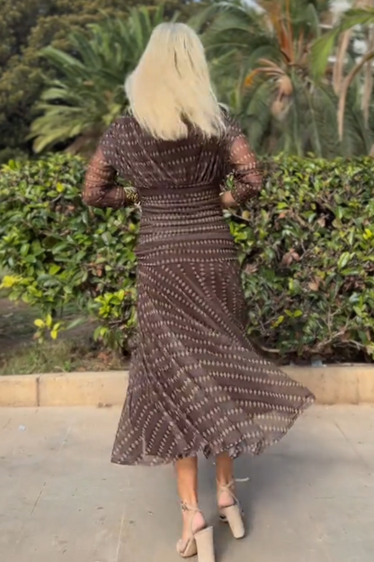 Brown - A woman smiling outdoors wearing an elegant, flowing brown maxi dress with a geometric diamond print, featuring a wrap-style V-neckline, sheer 3/4 sleeves, and a full skirt.