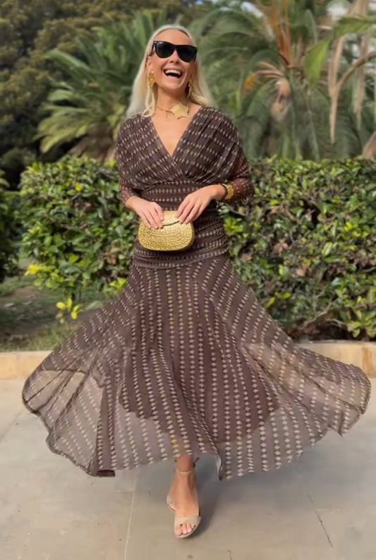 Brown - A woman smiling outdoors wearing an elegant, flowing brown maxi dress with a geometric diamond print, featuring a wrap-style V-neckline, sheer 3/4 sleeves, and a full skirt.