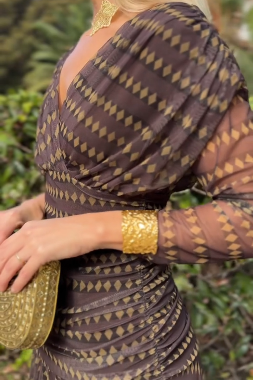 Brown - A woman smiling outdoors wearing an elegant, flowing brown maxi dress with a geometric diamond print, featuring a wrap-style V-neckline, sheer 3/4 sleeves, and a full skirt.