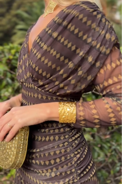 Brown - A woman smiling outdoors wearing an elegant, flowing brown maxi dress with a geometric diamond print, featuring a wrap-style V-neckline, sheer 3/4 sleeves, and a full skirt.