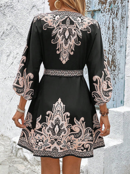 Black - Woman wearing a woven boho V-neck mini shirt dress with ornate paisley print and voluminous sleeves, holding a woven straw bag outdoors.