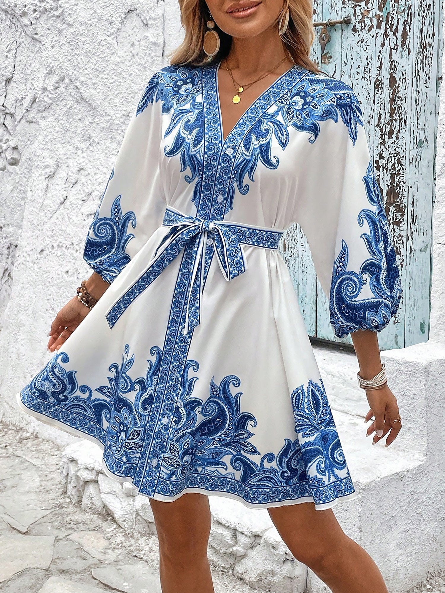 Blue - Woman wearing a woven boho V-neck mini shirt dress with ornate paisley print and voluminous sleeves, holding a woven straw bag outdoors.