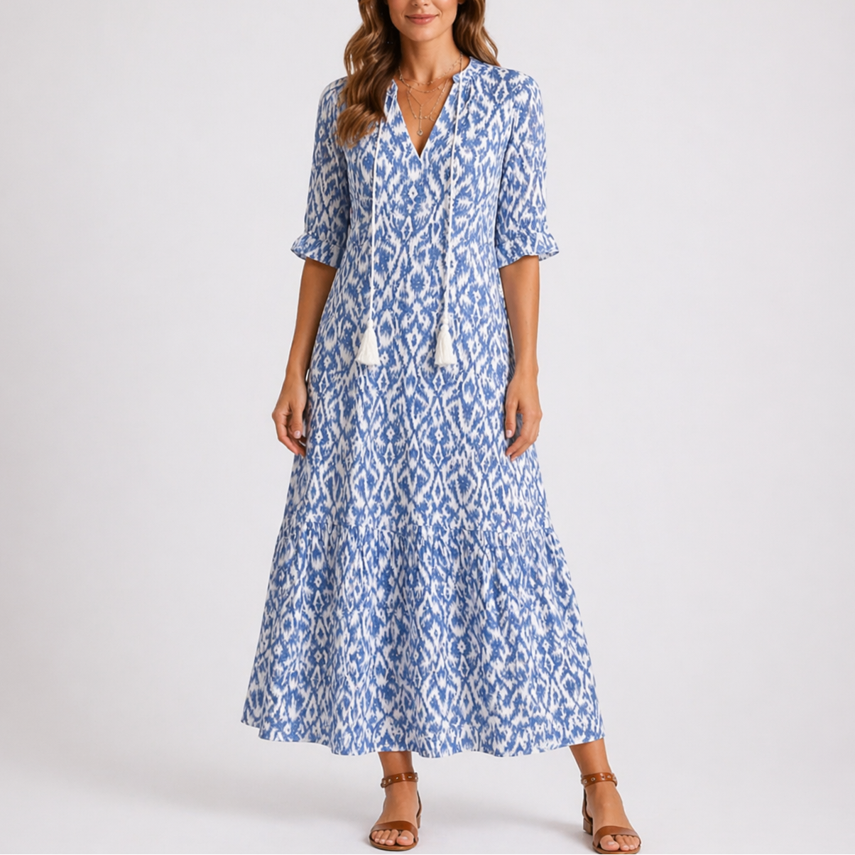 Blue - Model wearing a woven geometric ikat pattern maxi dress featuring a V-neckline with tassel ties, 3/4 sleeves, and a tiered hemline.