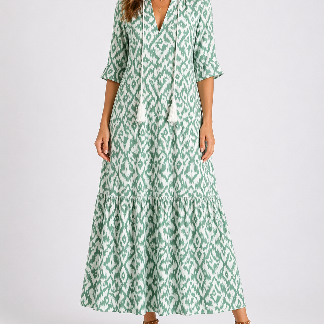 Light green - Model wearing a woven geometric ikat pattern maxi dress featuring a V-neckline with tassel ties, 3/4 sleeves, and a tiered hemline.