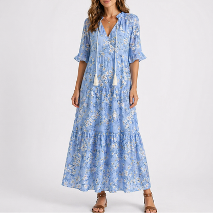 Blue & White - Model wearing a woven geometric ikat pattern maxi dress featuring a V-neckline with tassel ties, 3/4 sleeves, and a tiered hemline.