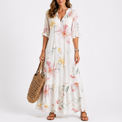 White - Model wearing a woven geometric ikat pattern maxi dress featuring a V-neckline with tassel ties, 3/4 sleeves, and a tiered hemline.