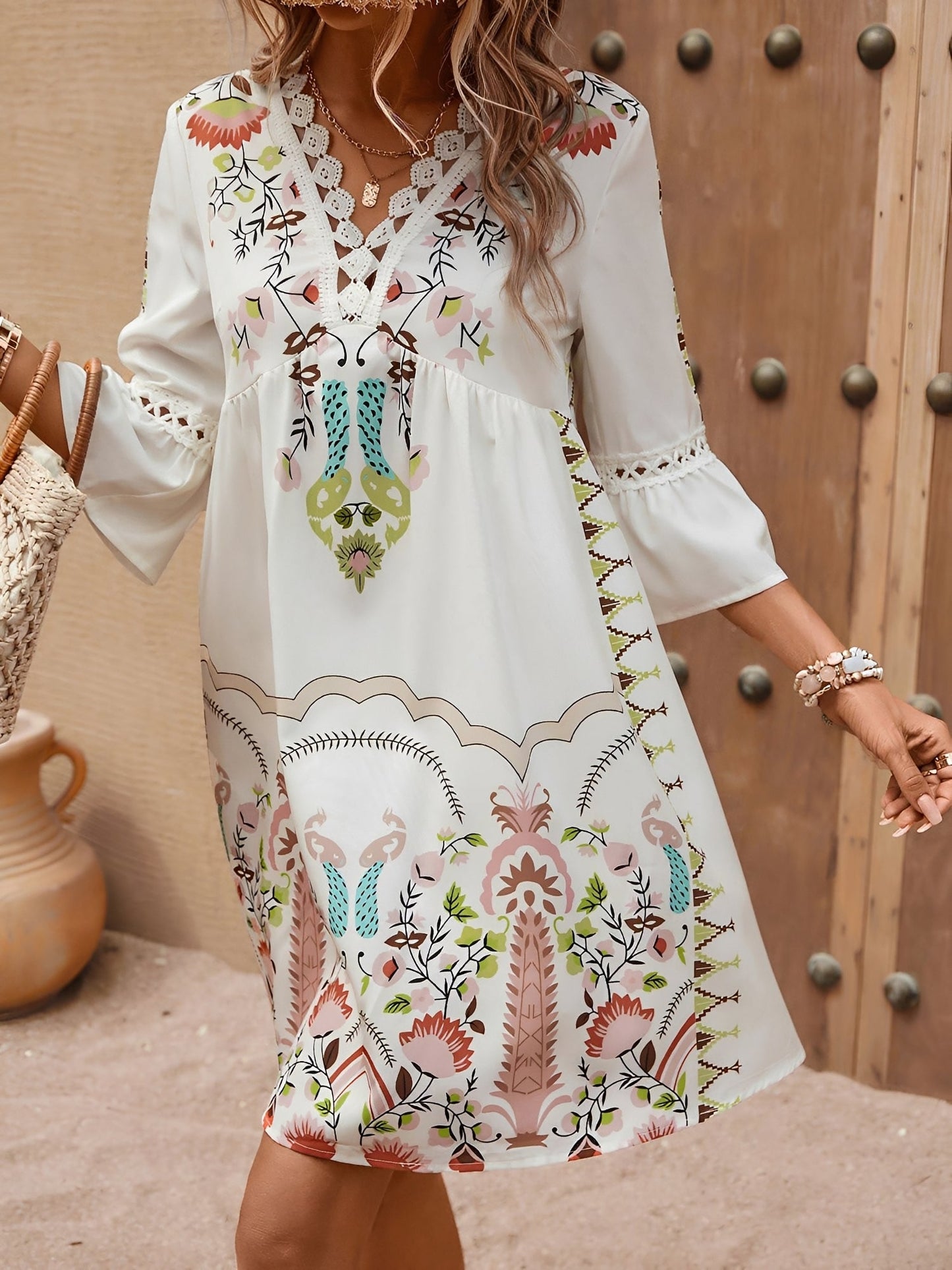 Apricot - Woman wearing a bohemian floral print V-neck tunic dress with crochet trim and three-quarter sleeves, styled with a straw hat and woven tote bag.