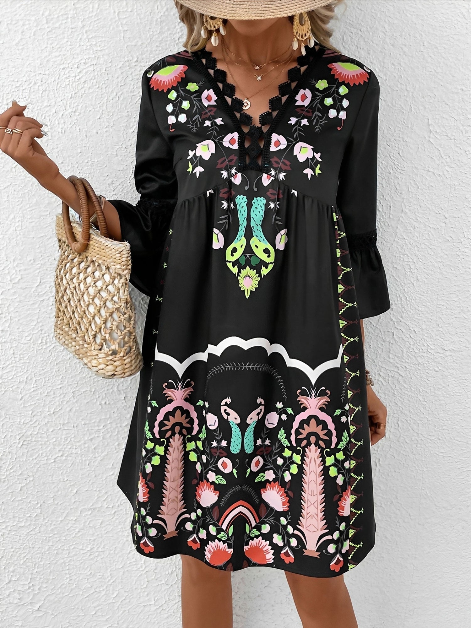 Black - Woman wearing a bohemian floral print V-neck tunic dress with crochet trim and three-quarter sleeves, styled with a straw hat and woven tote bag.