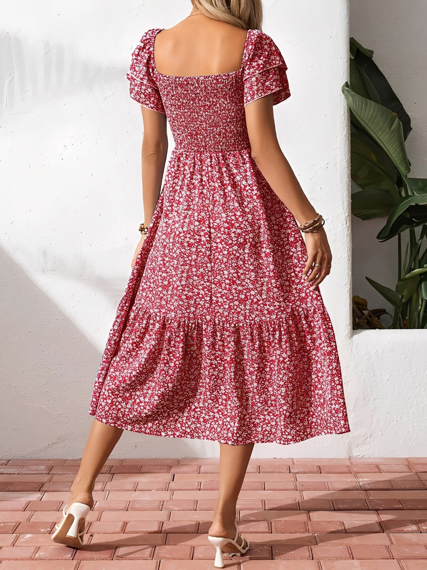 Red - Woman wearing a woven floral square-neck midi dress with a smocked bodice, flutter sleeves, and a tiered skirt, styled with a straw hat and woven bag.