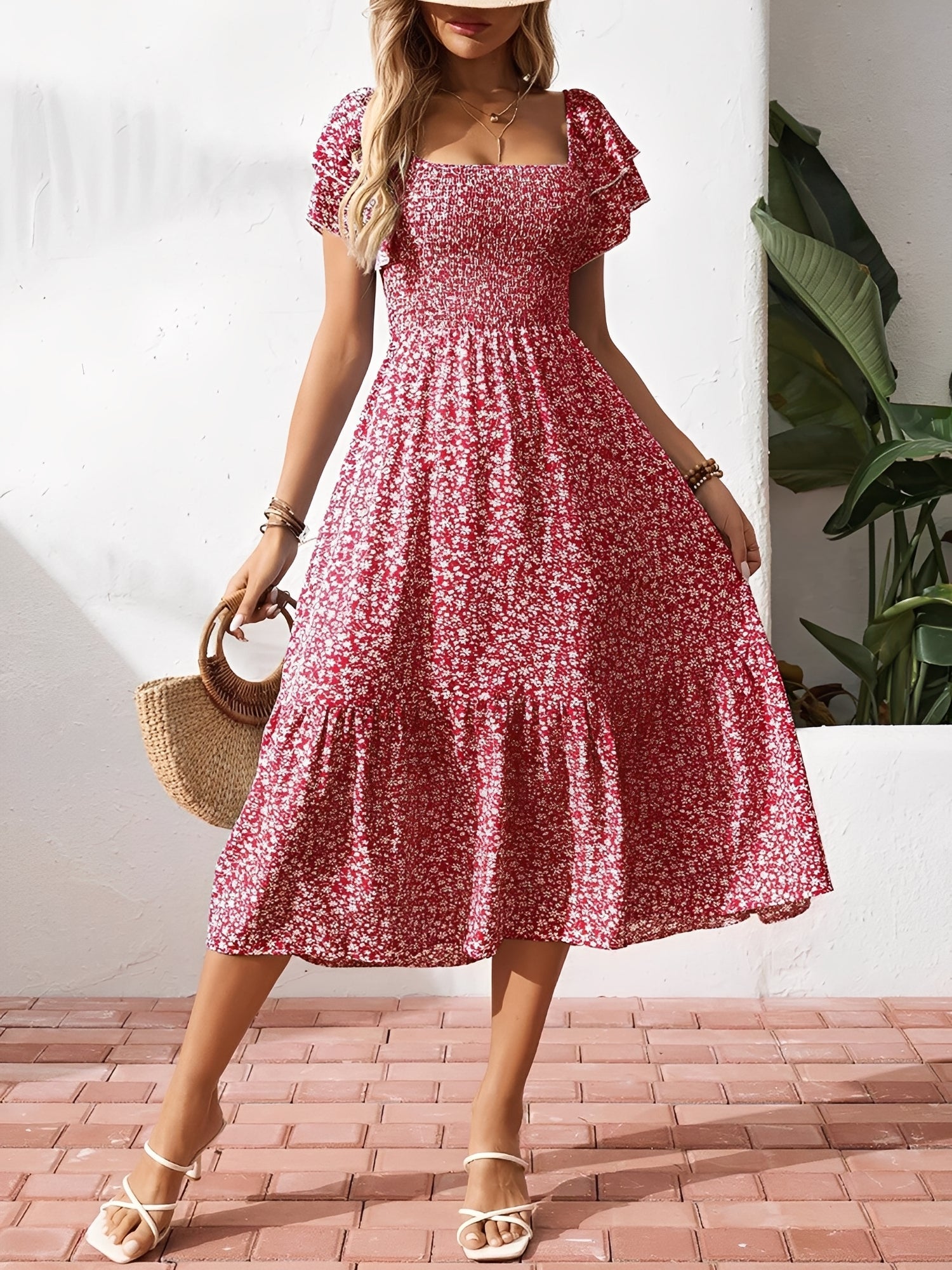 Red - Woman wearing a woven floral square-neck midi dress with a smocked bodice, flutter sleeves, and a tiered skirt, styled with a straw hat and woven bag.