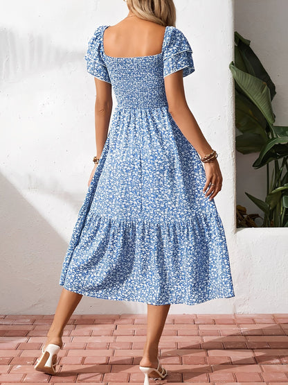 Blue - Woman wearing a woven floral square-neck midi dress with a smocked bodice, flutter sleeves, and a tiered skirt, styled with a straw hat and woven bag.