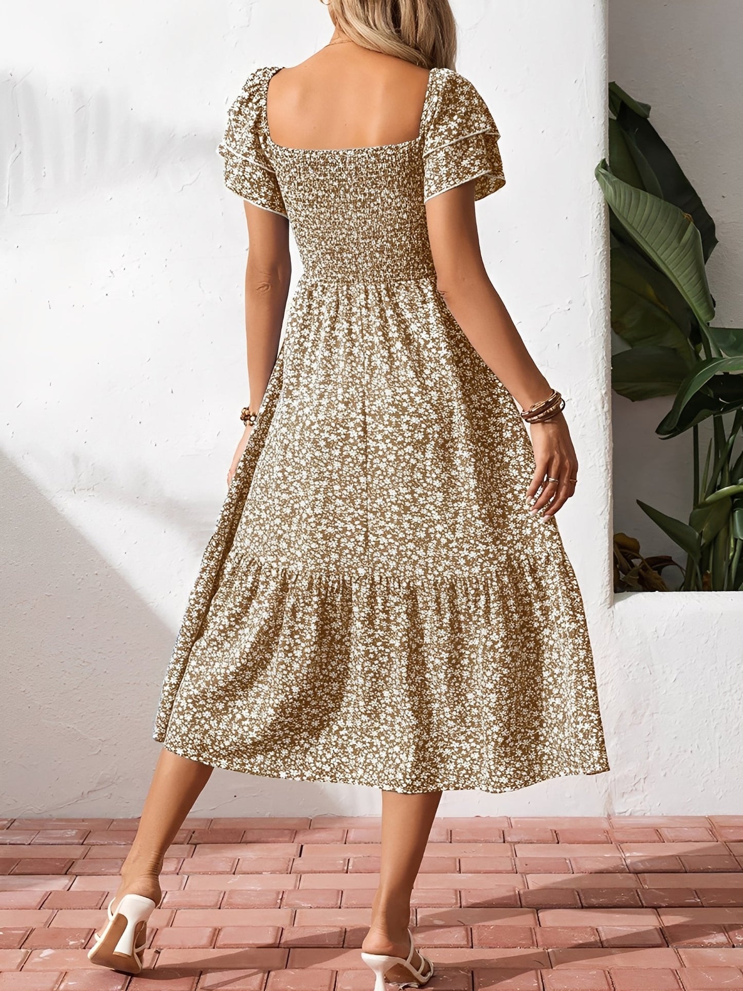 Khaki - Woman wearing a woven floral square-neck midi dress with a smocked bodice, flutter sleeves, and a tiered skirt, styled with a straw hat and woven bag.