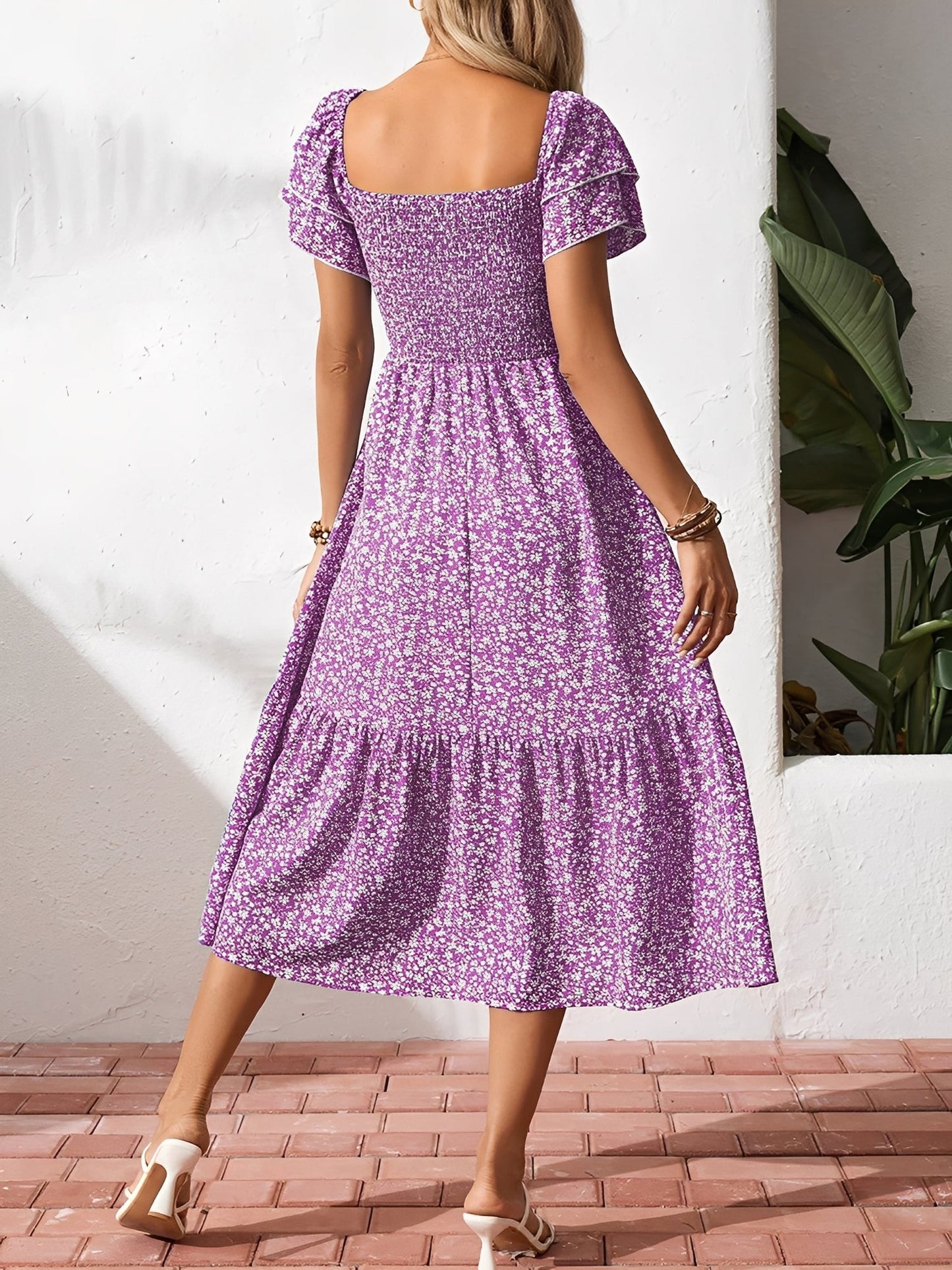 Blue - Woman wearing a woven floral square-neck midi dress with a smocked bodice, flutter sleeves, and a tiered skirt, styled with a straw hat and woven bag.