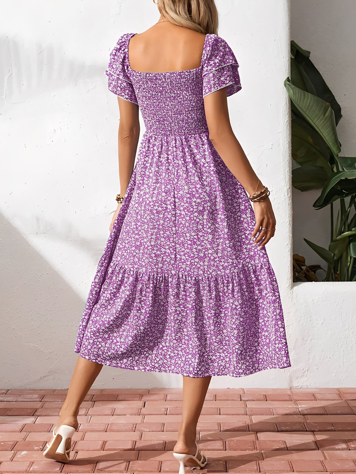 Blue - Woman wearing a woven floral square-neck midi dress with a smocked bodice, flutter sleeves, and a tiered skirt, styled with a straw hat and woven bag.