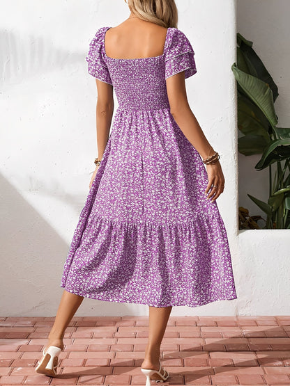 Blue - Woman wearing a woven floral square-neck midi dress with a smocked bodice, flutter sleeves, and a tiered skirt, styled with a straw hat and woven bag.