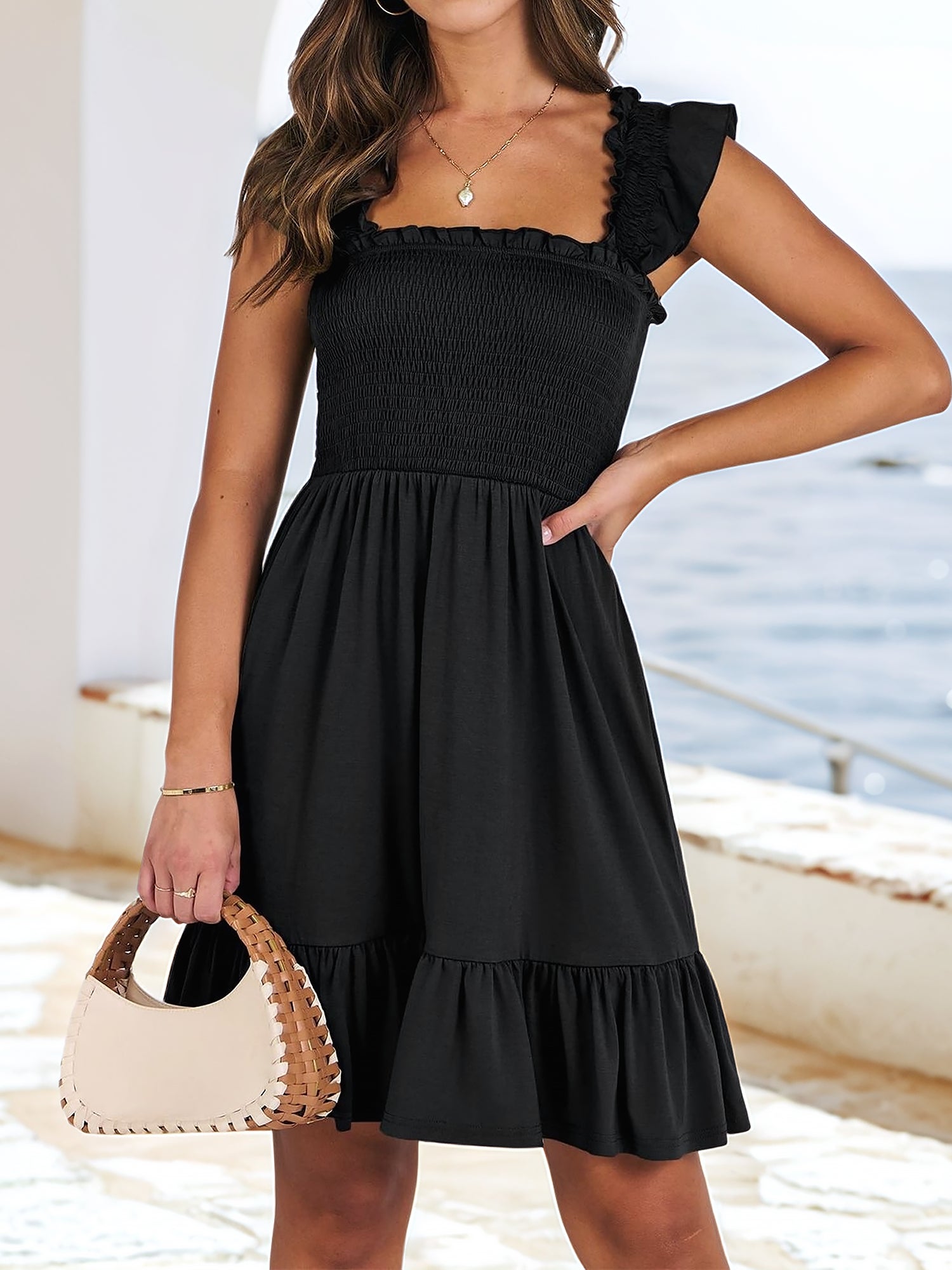 Black - Woman wearing a woven smock square-neck mini dress with flutter sleeves and a tiered ruffle hem, standing outdoors by the sea.