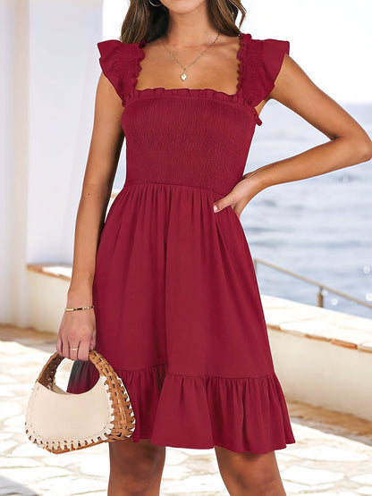 Burgundy - Woman wearing a woven smock square-neck mini dress with flutter sleeves and a tiered ruffle hem, standing outdoors by the sea.