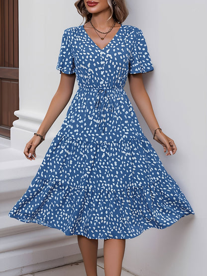 Blue - Woman wearing a spot pattern V-neck tiered midi dress with short sleeves and side pockets, standing in an architectural hallway.