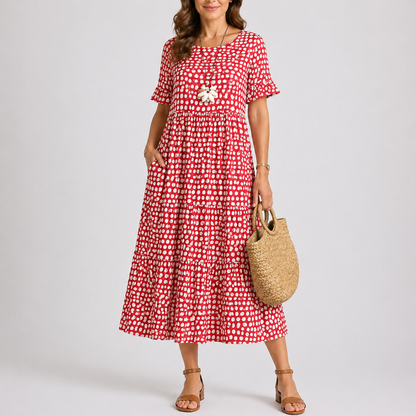 Red - Woman wearing a spotted short-sleeve tiered midi dress with side pockets, holding a woven bag.