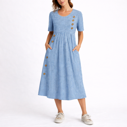 Blue - Woman wearing a striped short-sleeve midi dress with asymmetric wooden button detailing and side pockets, standing against a white background.