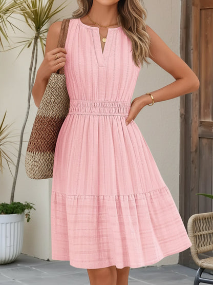 Pink - A woman wearing a sleeveless, textured woven midi dress with a notched V-neckline, shirred waist, and tiered skirt, holding a woven tote bag in a bright outdoor setting.