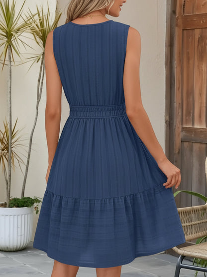 Dark Blue - A woman wearing a sleeveless, textured woven midi dress with a notched V-neckline, shirred waist, and tiered skirt, holding a woven tote bag in a bright outdoor setting.