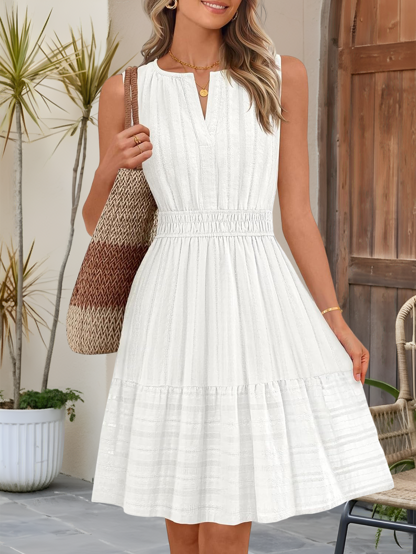 White - A woman wearing a sleeveless, textured woven midi dress with a notched V-neckline, shirred waist, and tiered skirt, holding a woven tote bag in a bright outdoor setting.