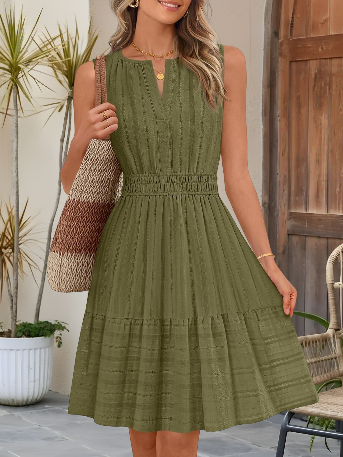 Olive Green - A woman wearing a sleeveless, textured woven midi dress with a notched V-neckline, shirred waist, and tiered skirt, holding a woven tote bag in a bright outdoor setting.